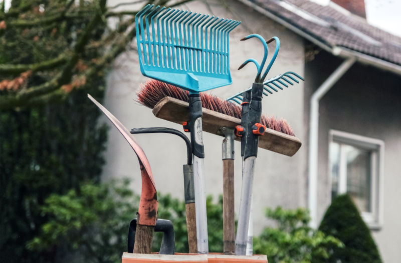 Konzept Hausmeisterservice: Besen, Rechen, Schaufeln und andere Werkzeuge für Haus und Garten in Nahaufnahme vor einem Haus